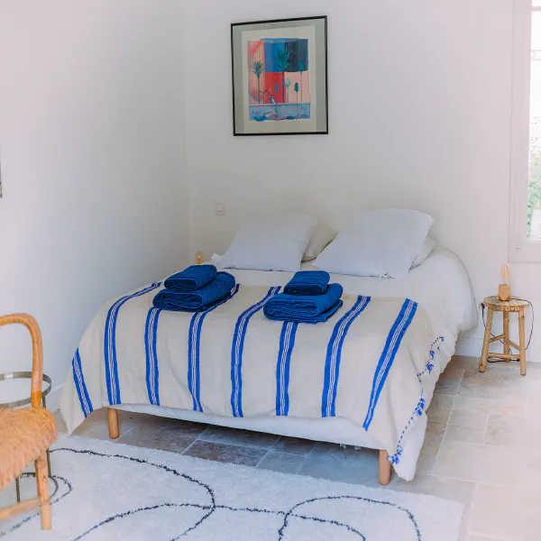 Chambre du gîte en pierre avec lit double, couverture rayée bleue et tableau coloré