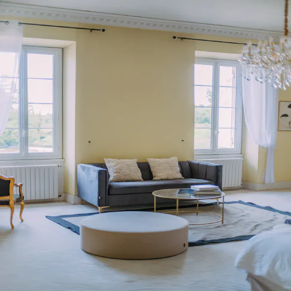 Suite spacieuse avec canapé velours gris et lustre cristal au Château de Laubardemont