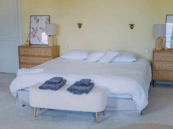Lit king-size avec serviettes, commodes cannées et appliques dorées au Château de Laubardemont