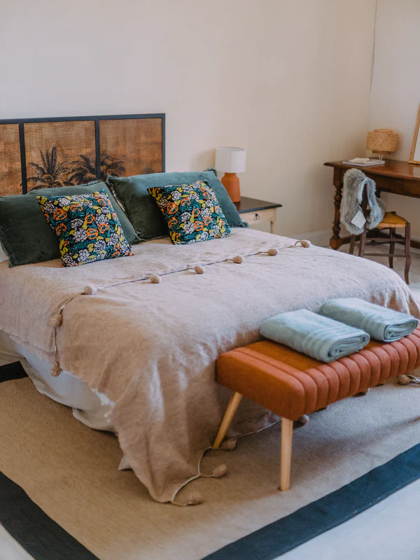 Chambre bohème avec lit double, tête de lit en cannage et coussins fleuris au château