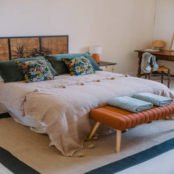 Chambre bohème avec lit double, tête de lit en cannage et coussins fleuris au château