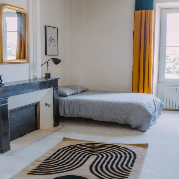 Chambre avec lit simple, cheminée noire, miroir doré et rideaux moutarde au château