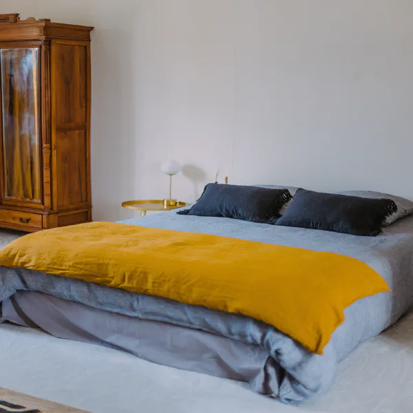 Lit double en lin gris avec plaid moutarde et armoire ancienne au Château de Laubardemont