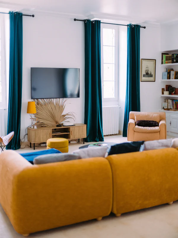 Salon lumineux avec canapé moutarde, rideaux bleu canard et bibliothèque au château