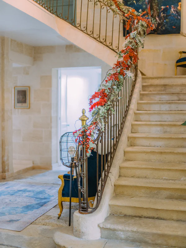 Escalier en pierre avec rampe fleurie et lustre en rotin au Château de Laubardemont