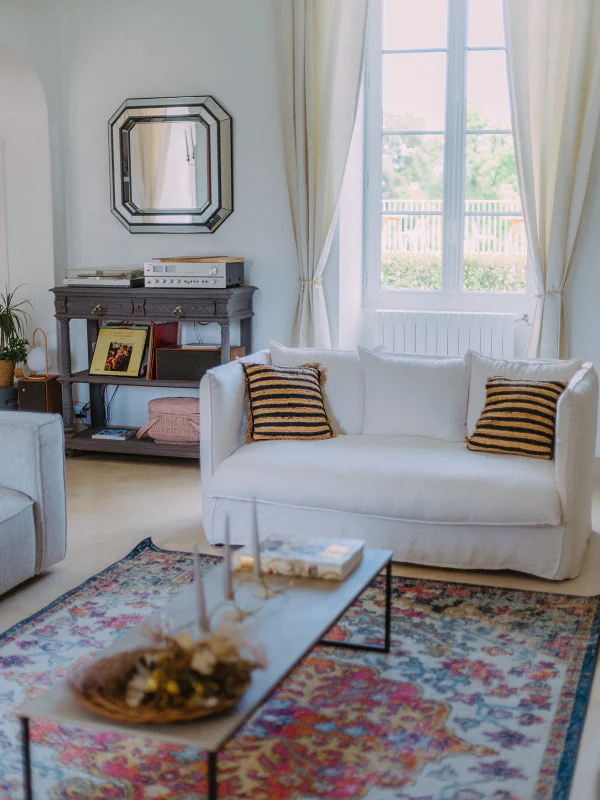 Salon blanc avec canapé houssé, tourne-disques et tapis bohème au Château de Laubardemont