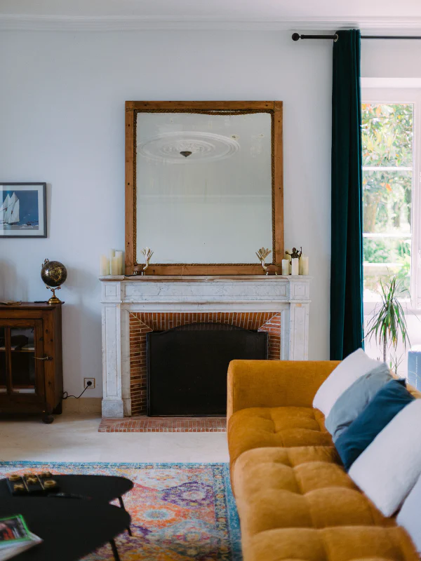 Cheminée en marbre blanc avec miroir ancien et canapé moutarde au Château de Laubardemont